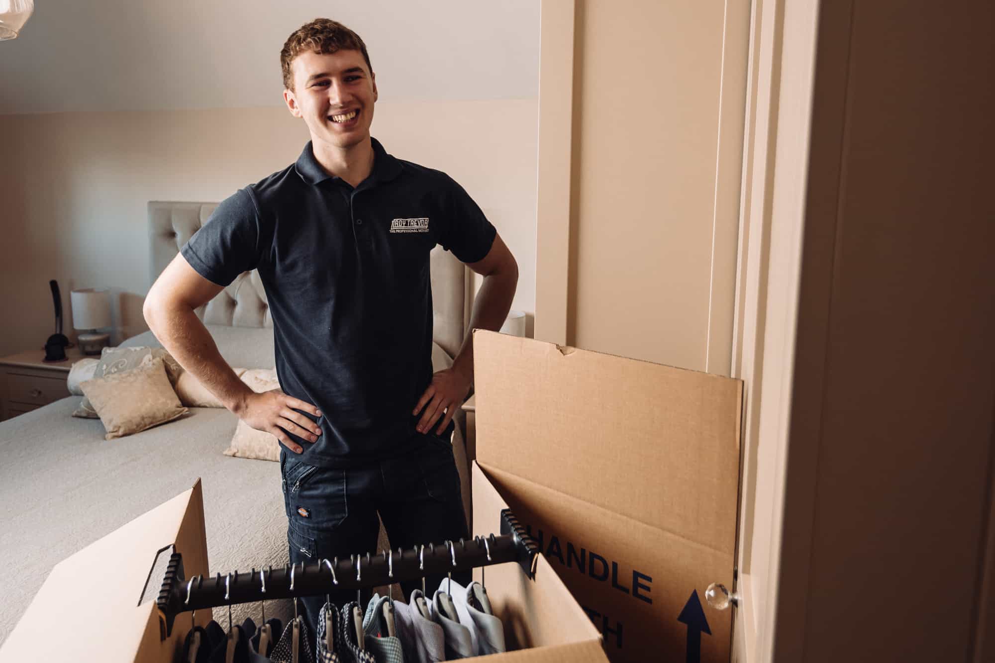 young man smiling after packing up clothes in cardboard wardrobe