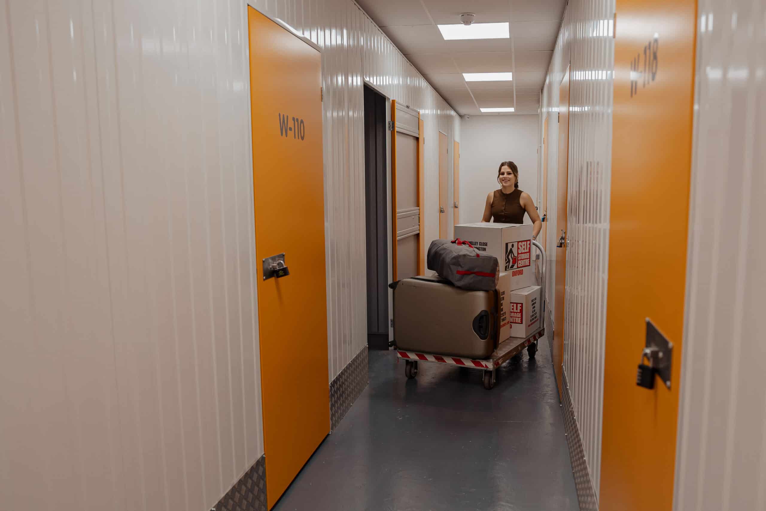 young lady pushing a trolley of boxes and suitcase at self storage centre