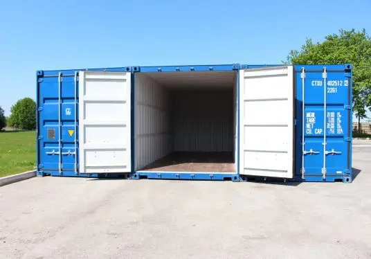 RT container storage An empty blue shipping container with both front doors wide open, placed on a paved surface outdoors under a clear blue sky.